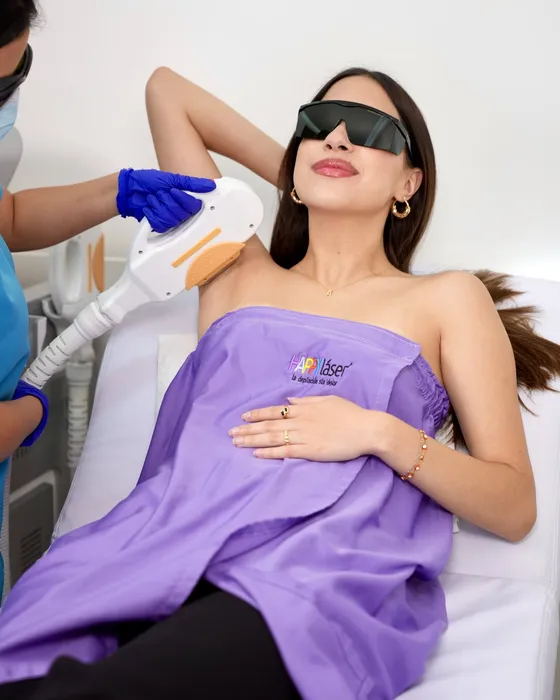 Clienta sonriente con gafas de protección durante una sesión de depilación láser en la axila