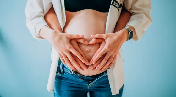 Manos formando un corazón sobre la barriga de una mujer embarazada
