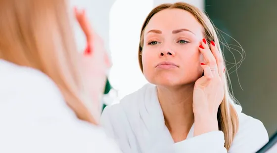 Mujer revisando la piel de su rostro frente al espejo