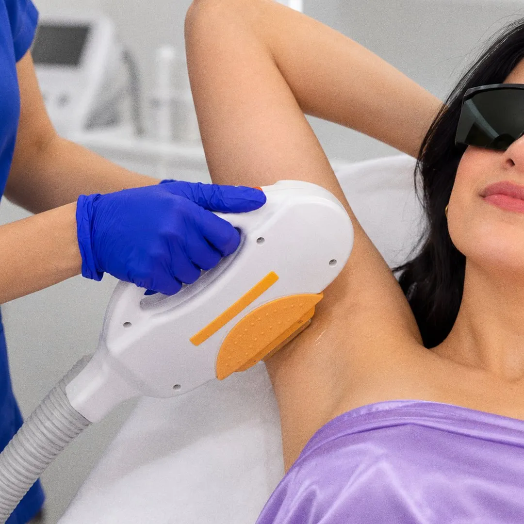 Especialista con guantes aplicando el cabezal del láser en la axila de una clienta con gafas de protección